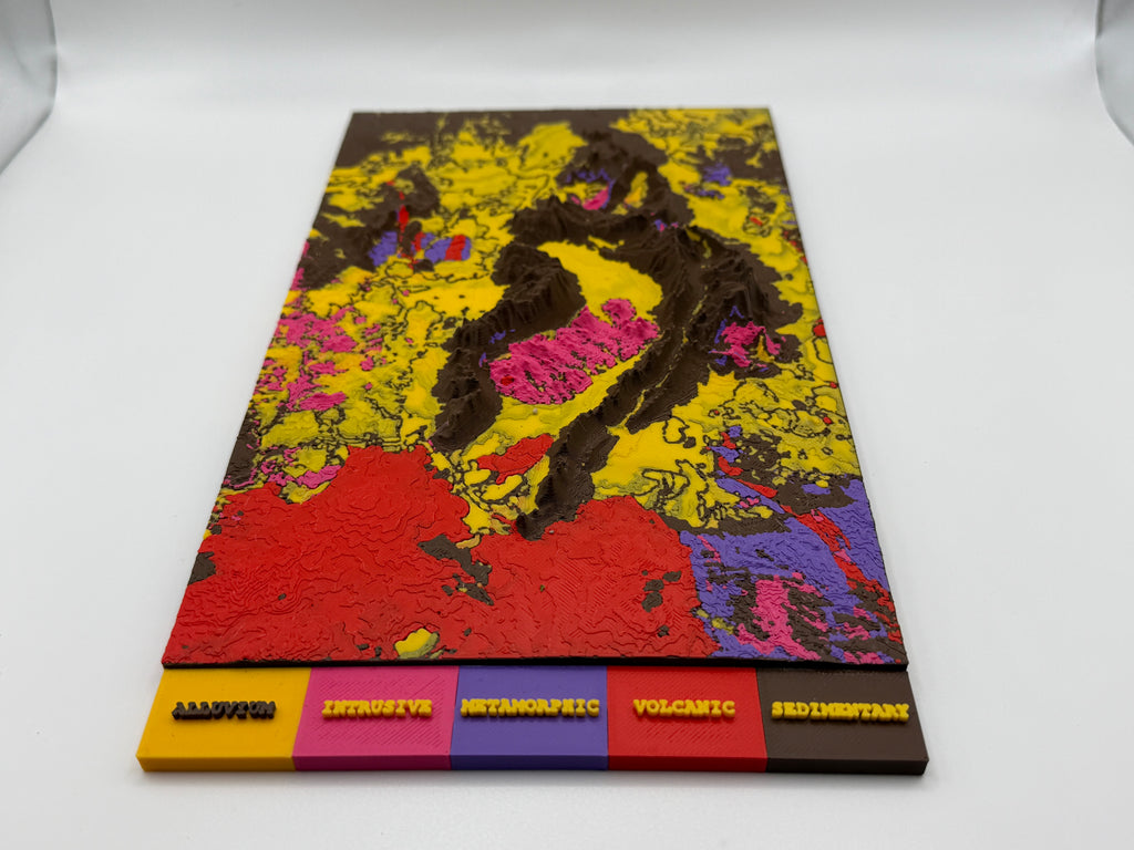 A rectangular 3D relief map model of the Earth's crust, featuring textured mountainous landforms in yellow, red, pink, brown, and purple. The base is labeled with color-coded categories: 'MASSIVE', 'INTROACTIVE', 'METAMORPHIC', 'VOLCANIC', and 'SEDIMENTARY' in raised 3D letters.